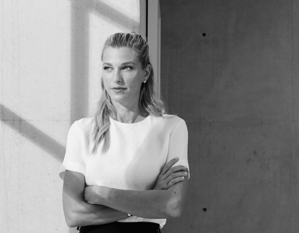 Nicole Junkermann in an ivory blazer with arms crossed against a concrete wall