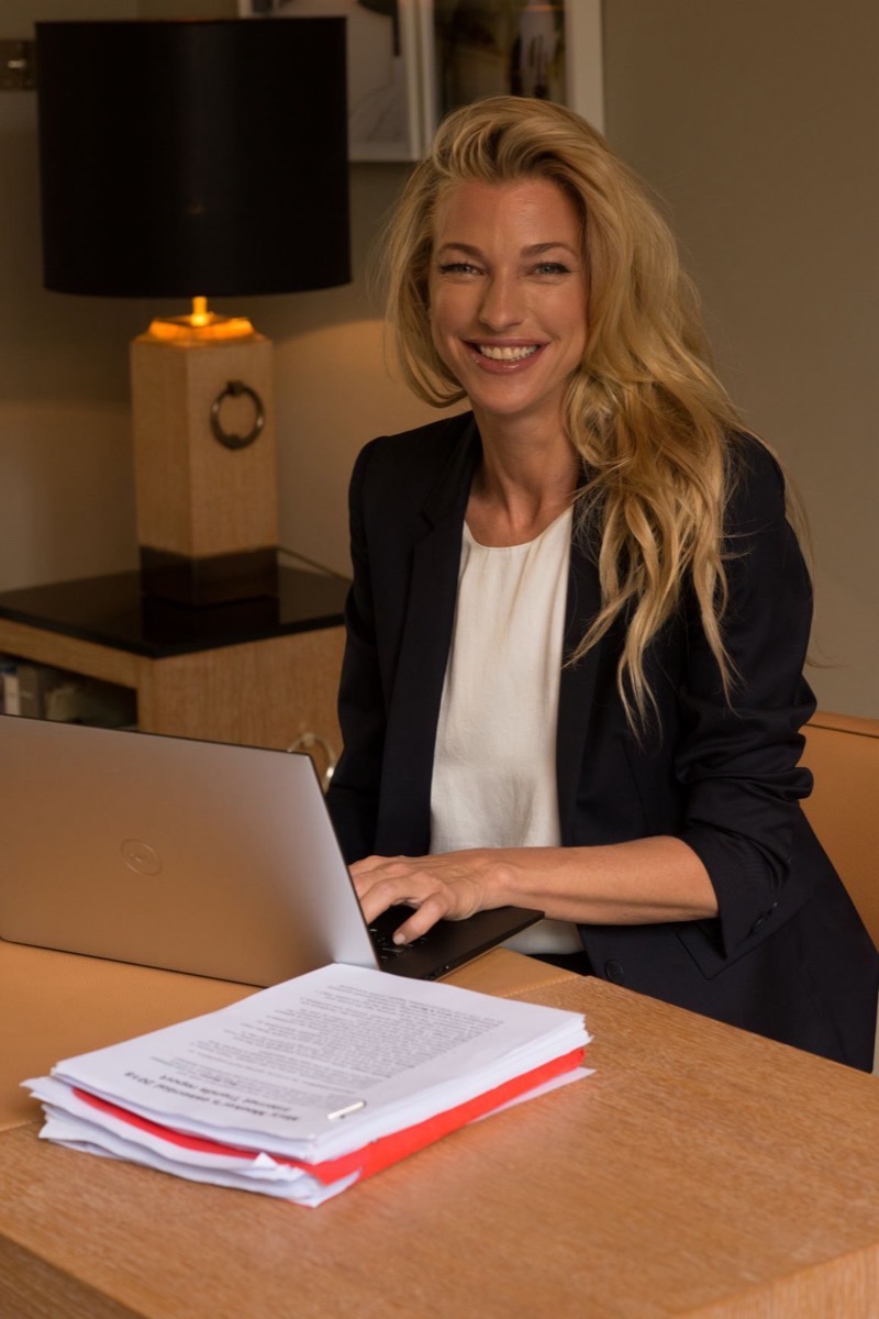 Nicole Junkermann in a navy blazer writing at a lamp-lit desk with a laptop