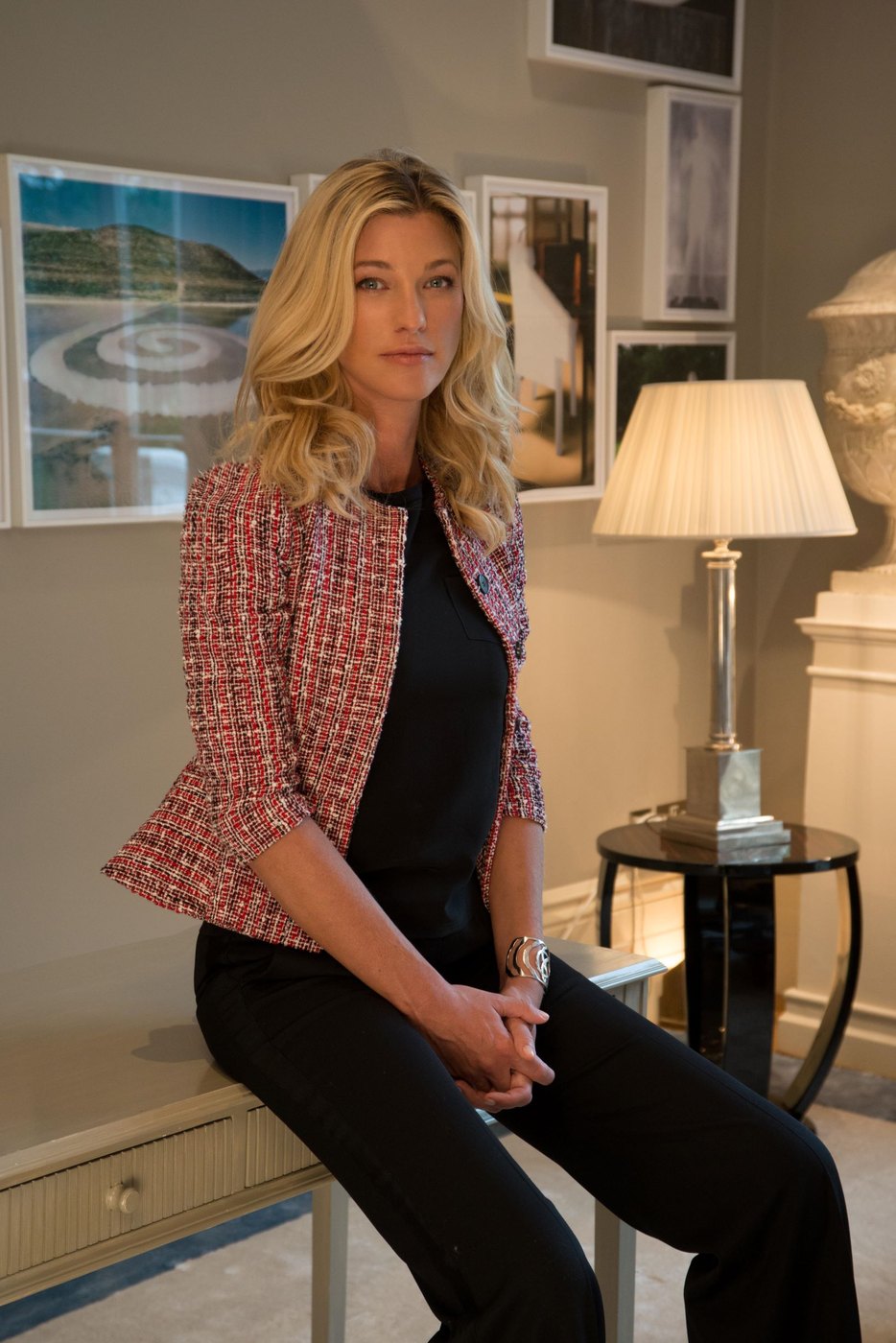 Nicole Junkermann seated in a tweed jacket in a bright sitting room with framed pictures on the wall behind her